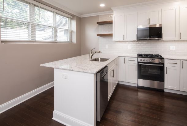 Modern kitchen with white cabinets, marble countertop, dark wood floor, and stainless steel appliances.