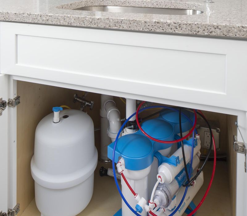 Under-sink reverse osmosis water filtration system with blue and white canisters and connected tubes.
