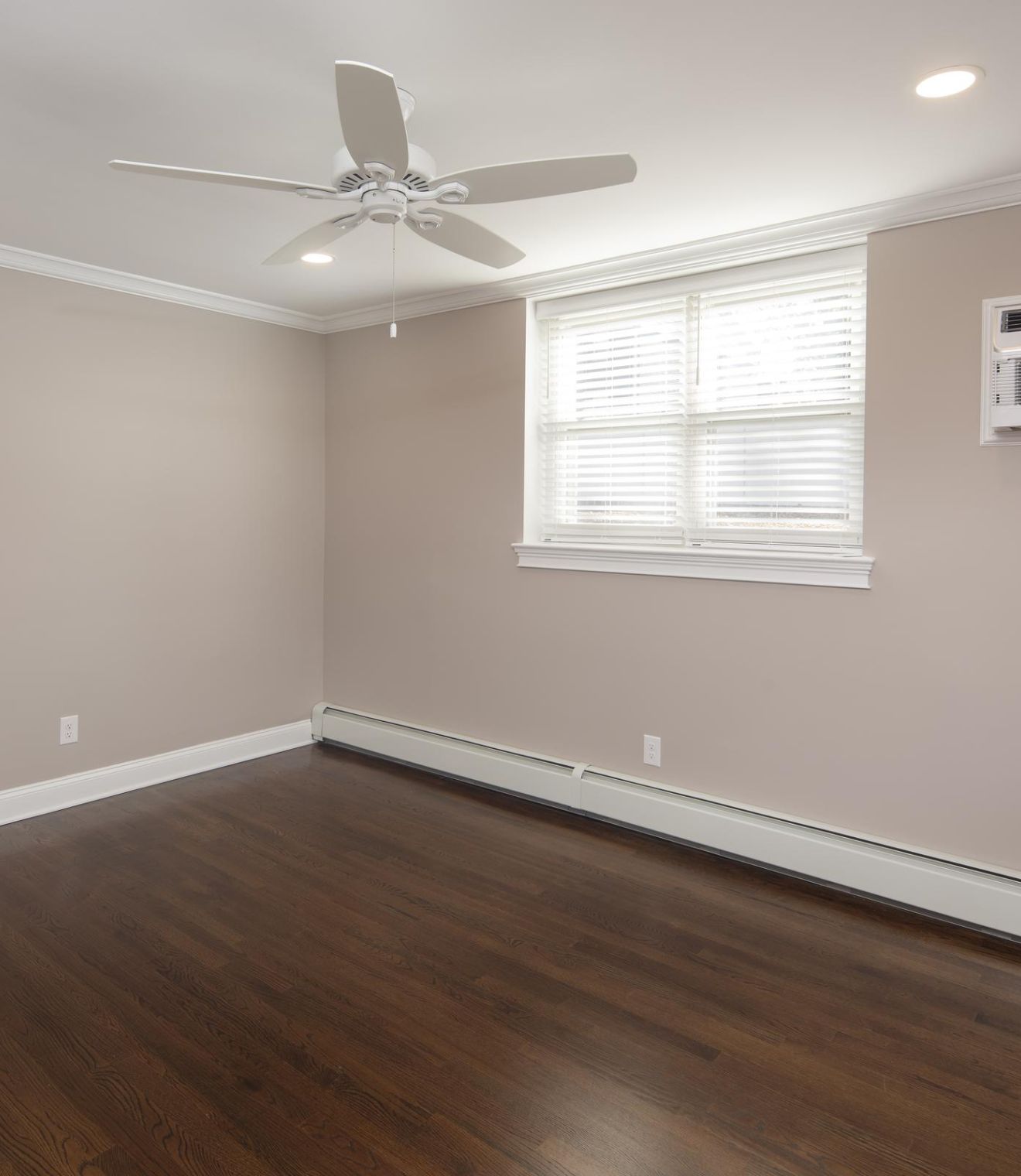 A bright bedroom with a neatly made bed, two bedside tables, lamps, and a window letting in natural light.