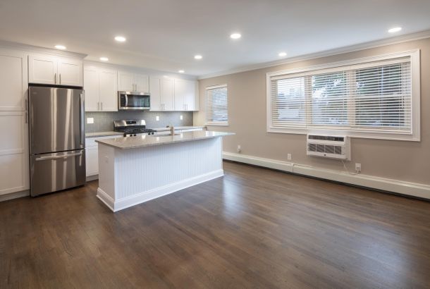 Modern kitchen with white cabinets, stainless steel appliances, island, and hardwood floors in a bright room.