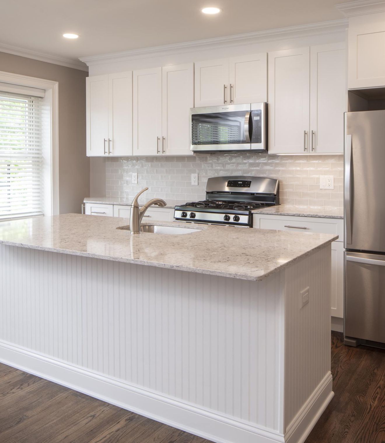 Modern kitchen with white cabinets, stainless steel appliances, and a marble island with three stools.