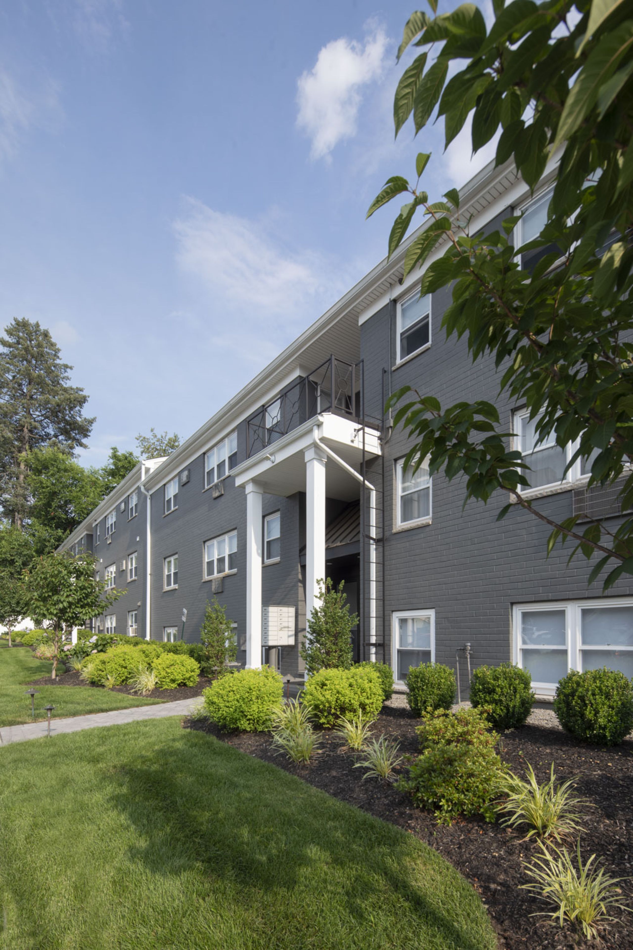 Woodland Hills Manor A modern apartment building with landscaped gardens and a wooden entrance canopy under a partly cloudy sky.