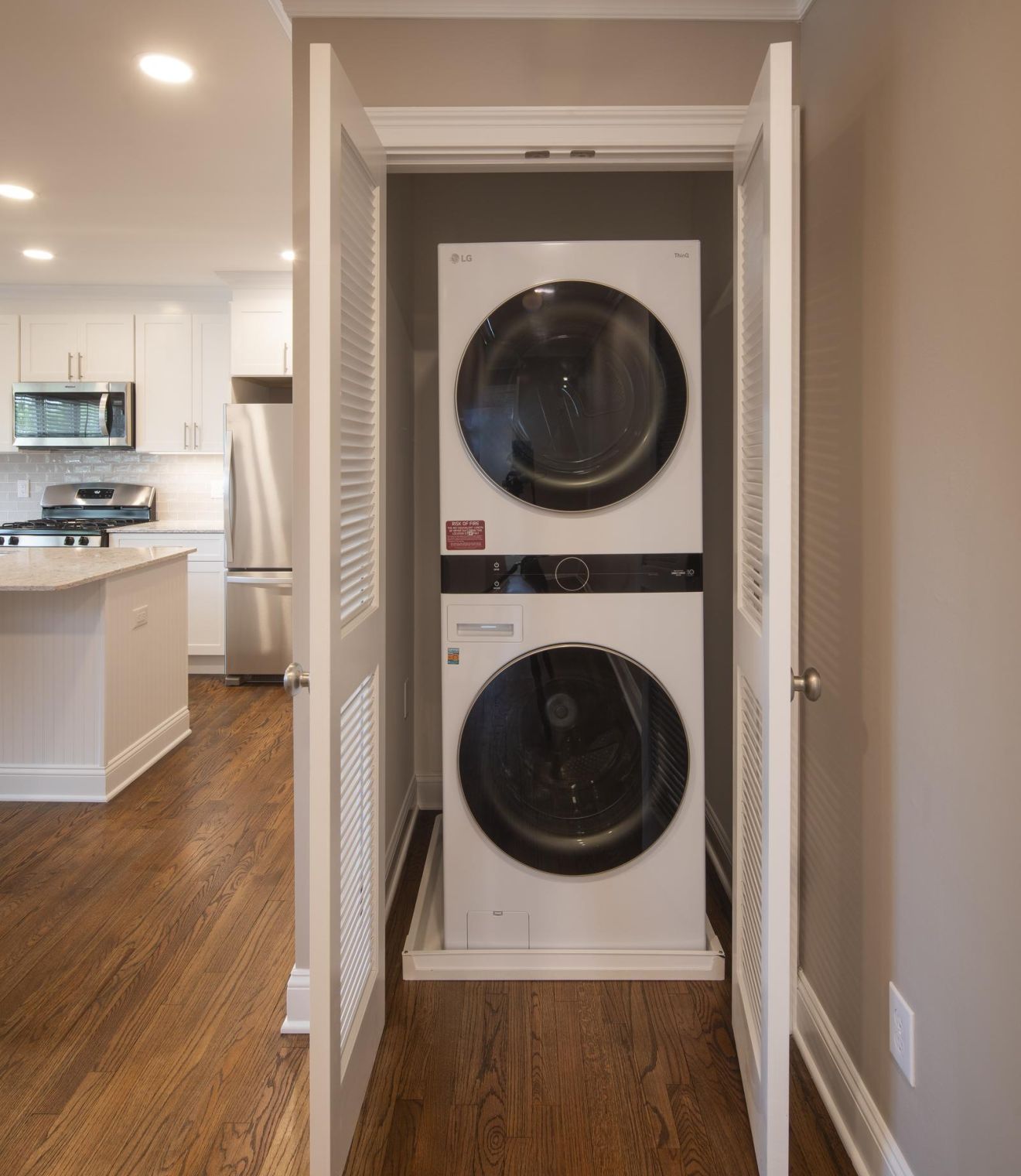 Stacked washer and dryer in a laundry room with a view into a bathroom through an open door.