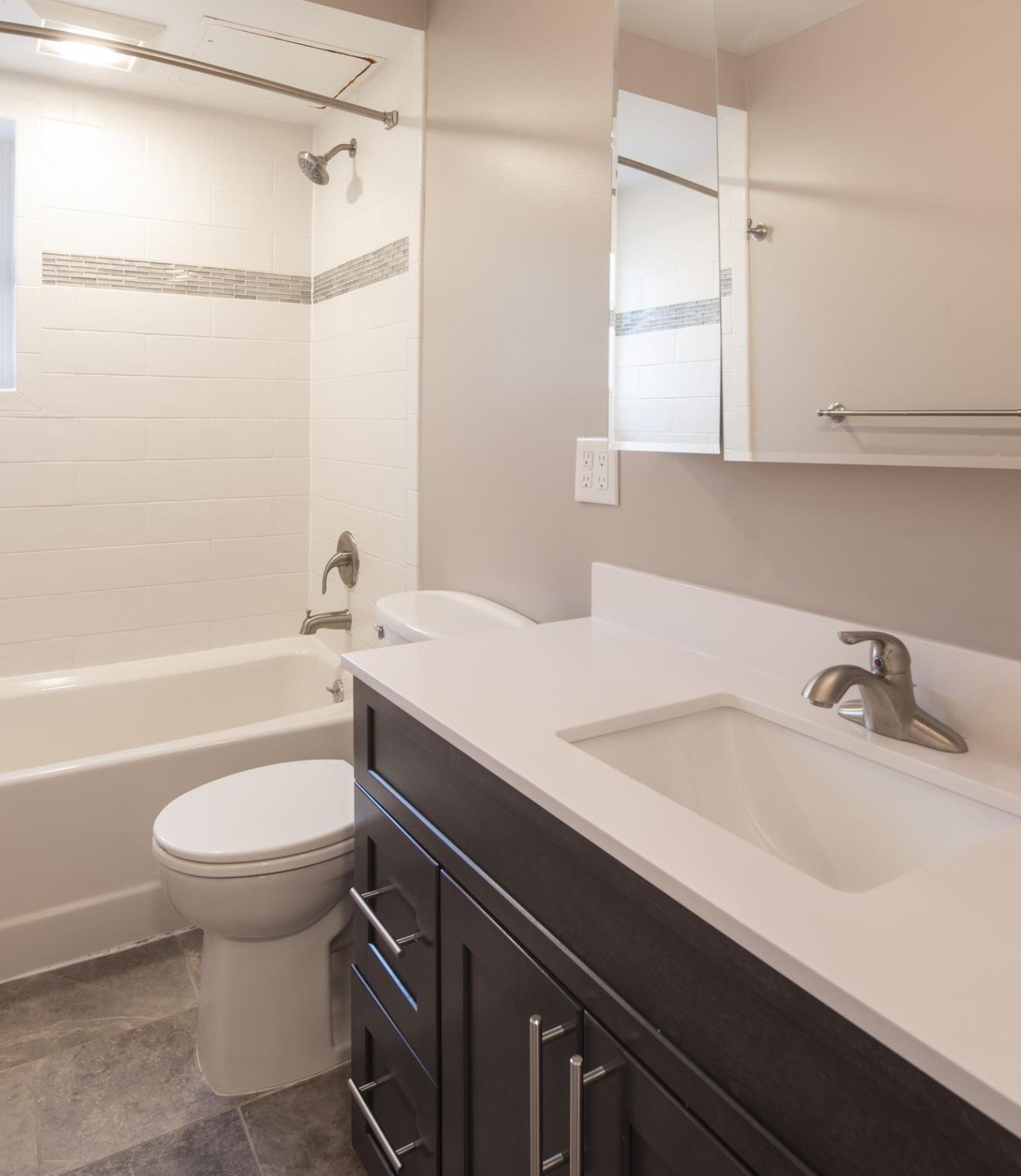 Modern bathroom with dark wood vanity, white countertop, mirror cabinet, and bathtub with white shower curtain.