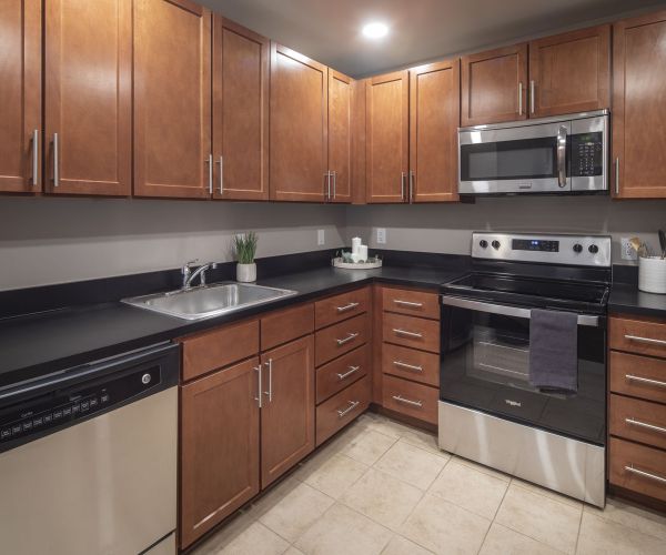 Modern kitchen with wooden cabinets, black countertops, stainless steel appliances, and tiled floor.