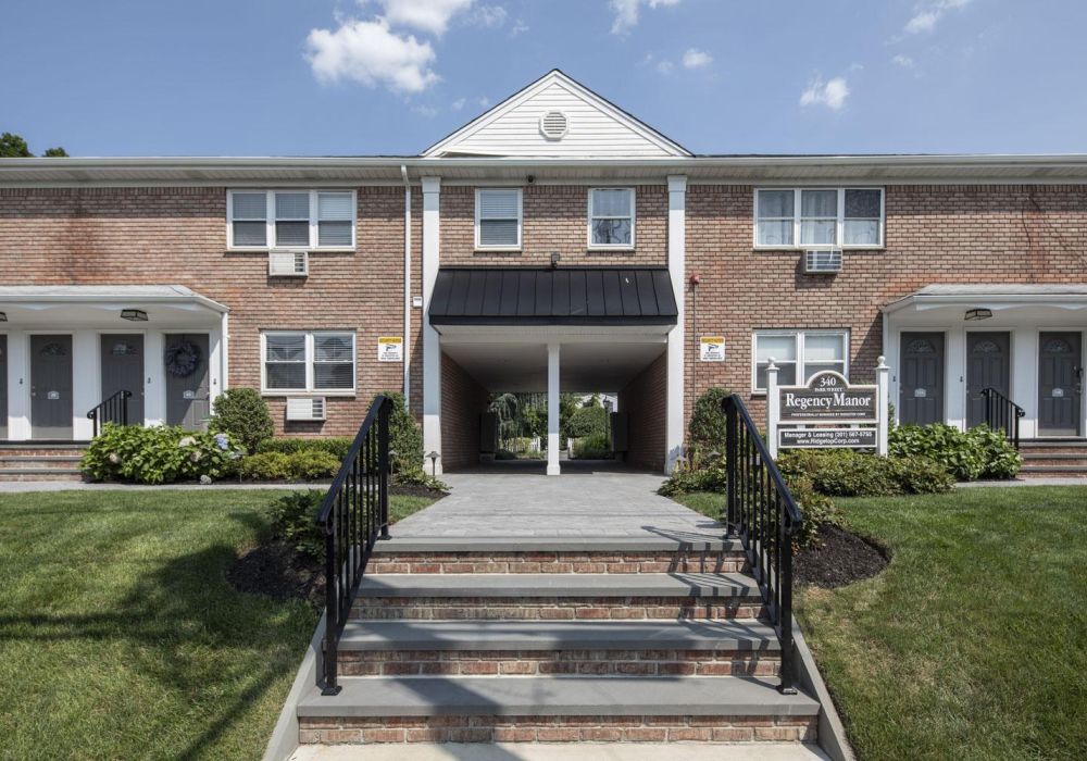 Two-story brick apartment building with central entryway, stairs, and a sign reading "Regency Manor.