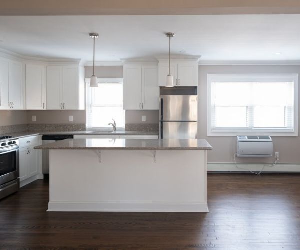 Modern kitchen with white cabinets, stainless steel appliances, island, and hardwood floors.