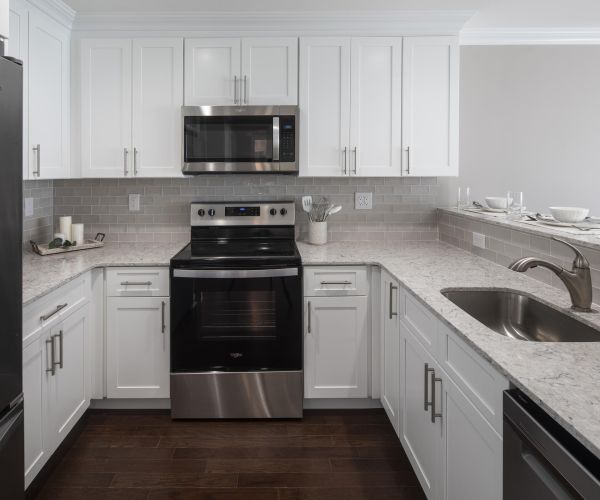 Modern kitchen with white cabinets, stainless steel appliances, and a marble countertop with a sink.