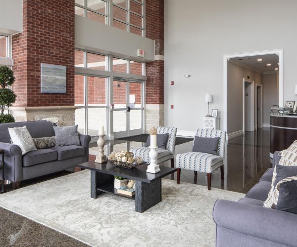 Modern lobby with gray sofas, armchairs, a coffee table, plants, and large windows letting in natural light.
