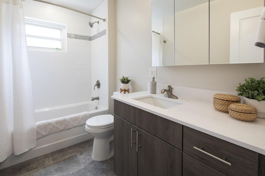 Ridgetop Modern bathroom with a bathtub, shower curtain, white countertop, dark vanity, and decorative plants.