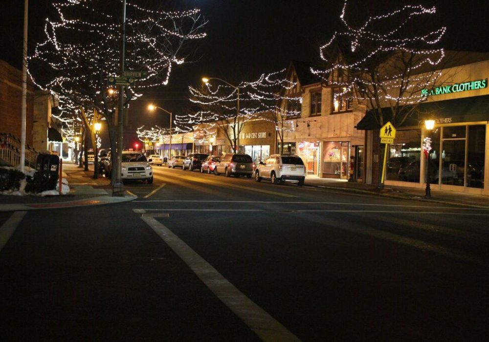 Downtown Westwood street at night with trees and storefronts decorated with white holiday string lights.