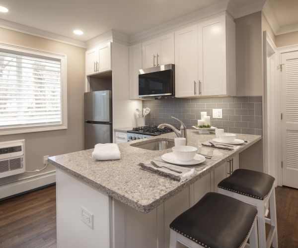 Modern kitchen with granite countertops, white cabinets, and a breakfast bar set for three with stools.