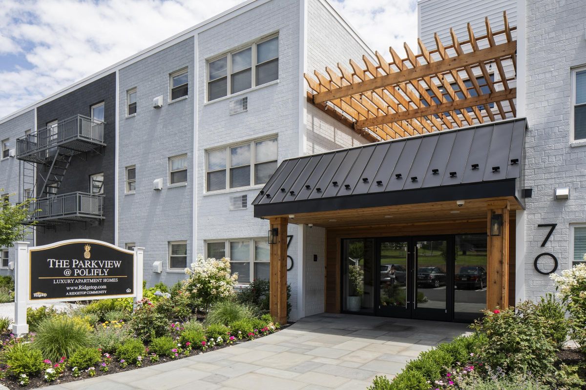 Entrance to a modern apartment building with a black awning and landscaped garden, sign reads "The Parkview at Folly".