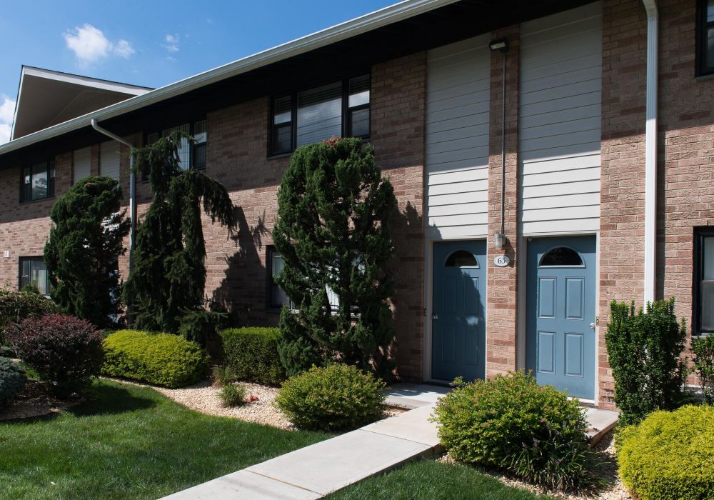 Two blue entrance doors on a brick apartment building with green shrubs and trees in front.