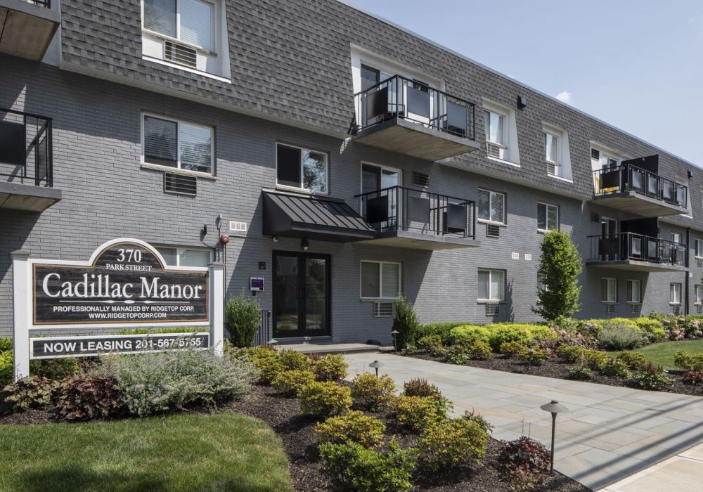 Gray brick apartment building with balconies and a "Cadillac Manor" sign, now leasing modern apartments.