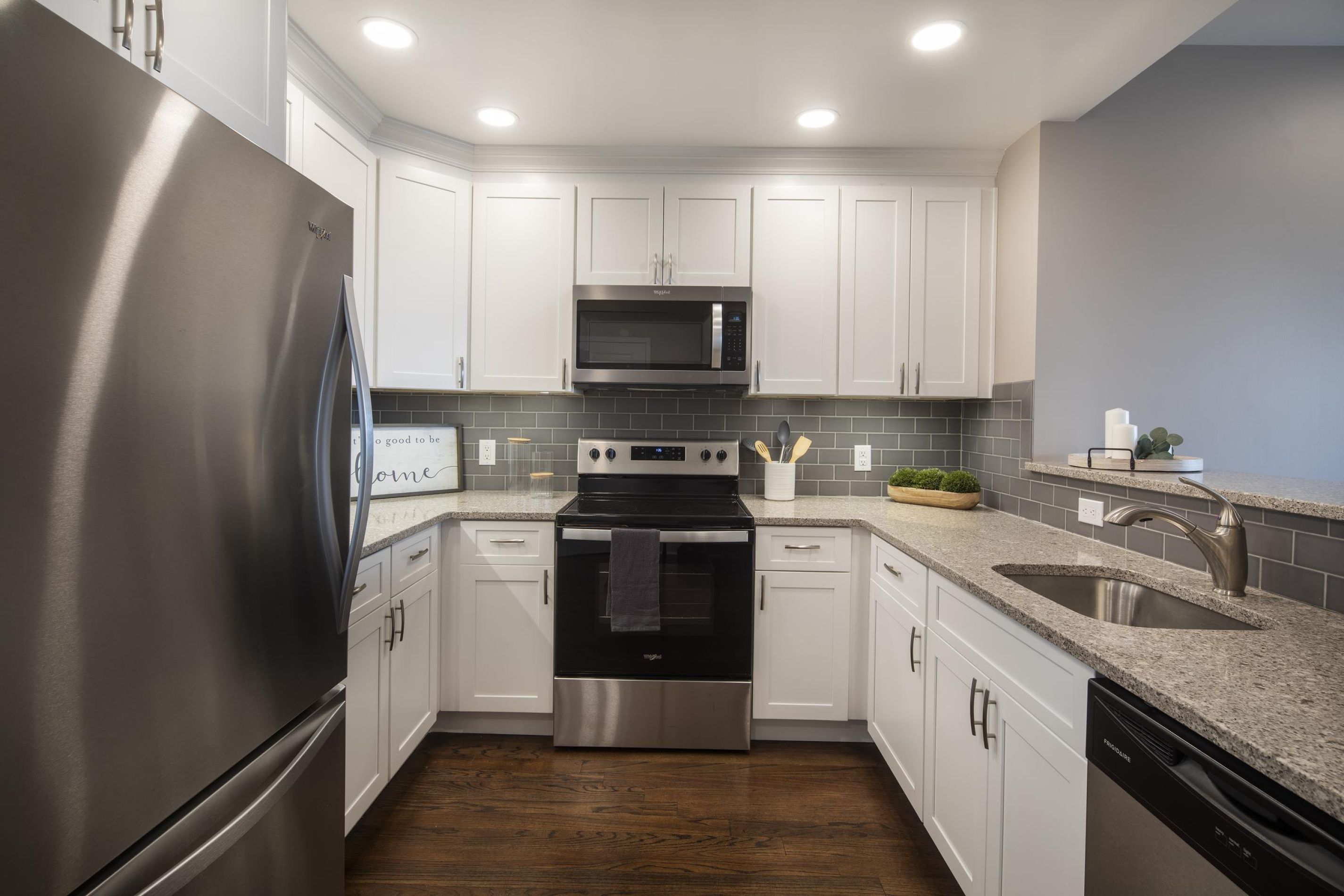Modern kitchen with white cabinets, stainless steel appliances, gray tile backsplash, and granite countertops.
