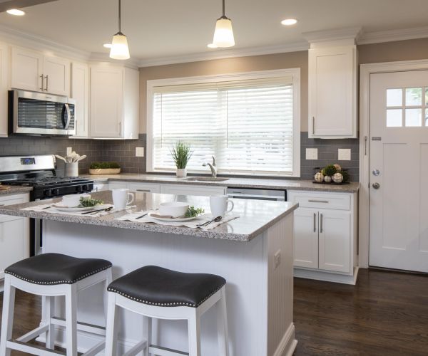 Modern kitchen with white cabinets, gray countertops, an island with stools, and a window letting in sunlight.