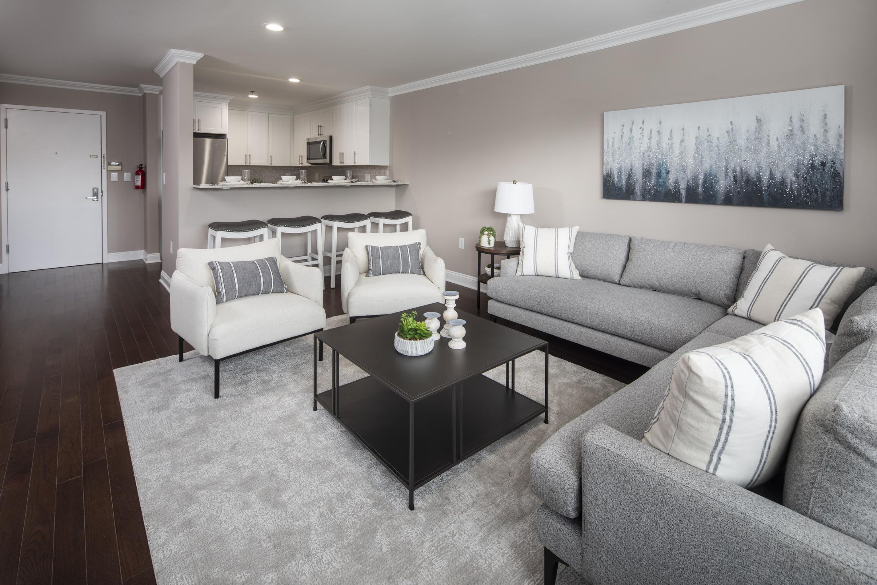 Modern living room with gray sofa, armchairs, coffee table, and open kitchen in the background.