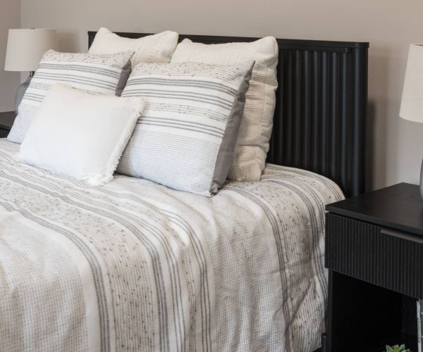 Modern bedroom with a neatly made bed, striped bedding, pillows, and two lamps on black nightstands.