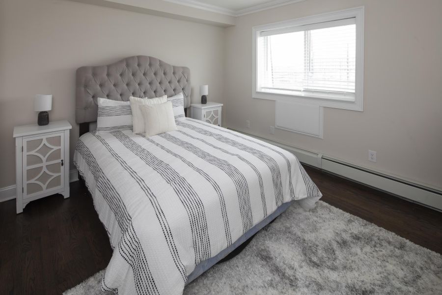 Ridgetop A neatly made bed with striped bedding, two nightstands, lamps, and a window in a bright bedroom.