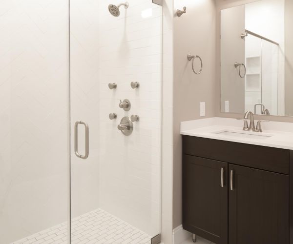 Modern bathroom with a glass shower, white tile, and a Hickory vanity with a sink and mirror on North Washington Square.
