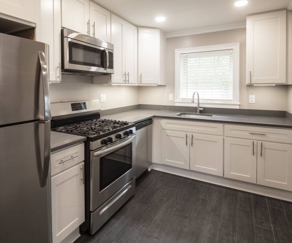 Modern kitchen with stainless steel appliances, white cabinets, and dark wood flooring.