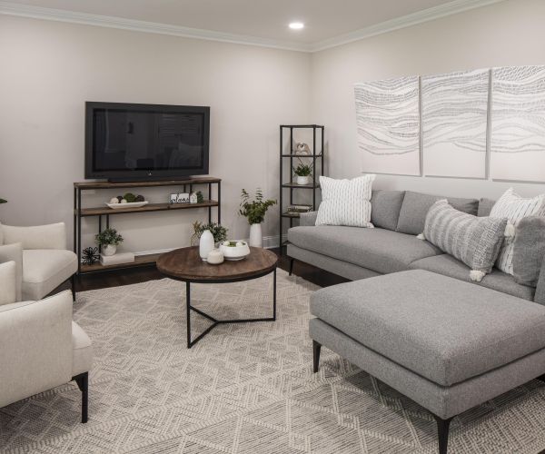Modern living room with a gray sectional sofa, round coffee table, TV, and neutral decor accents.
