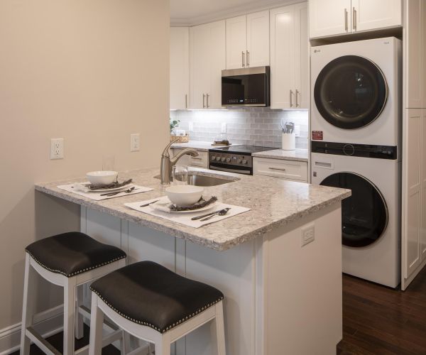 Modern kitchen with white cabinets, stacked washer and dryer, and a small island with two place settings.
