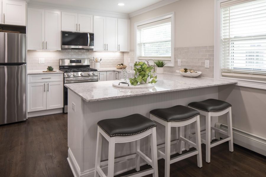 Ridgetop Modern kitchen with white cabinets, marble island, three stools, stainless steel appliances, and bright lighting.