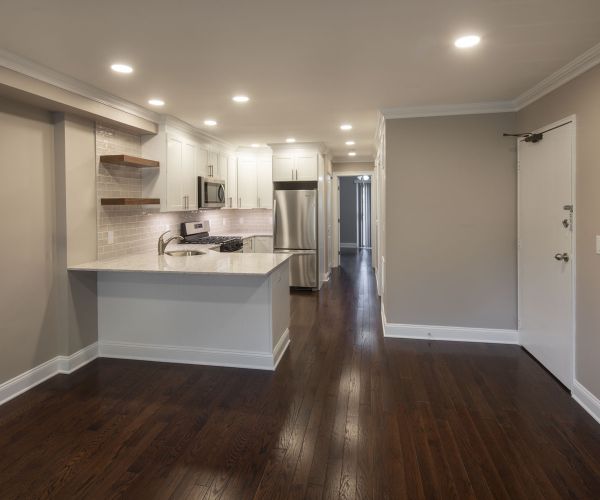 Modern kitchen with white cabinets, stainless steel appliances, and dark hardwood floors in open layout.