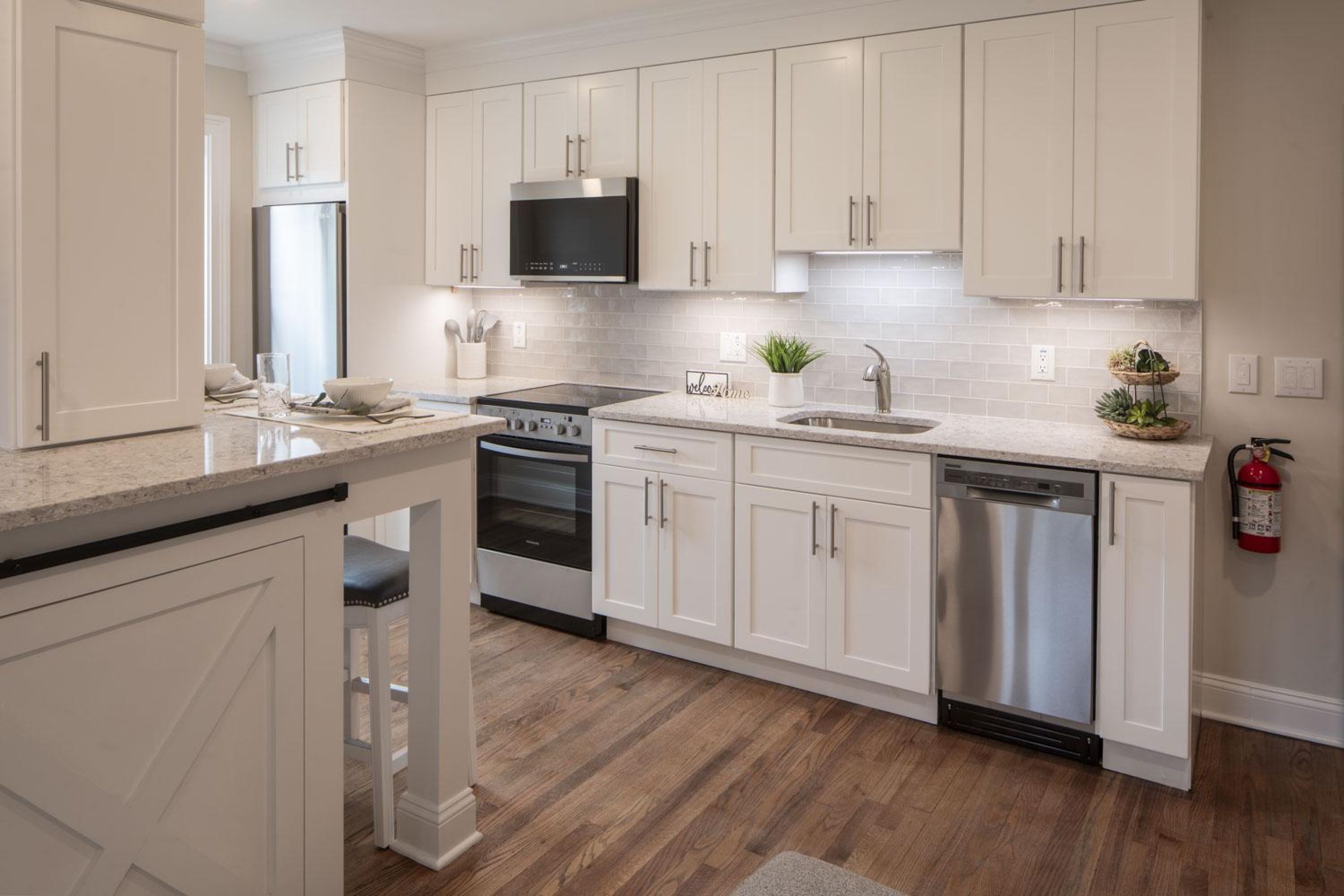 Modern kitchen with white cabinets, stainless steel appliances, and a light gray countertop on wood floors.