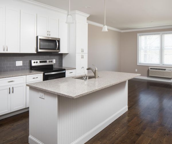Modern kitchen with white cabinets, stainless steel appliances, and a center island, next to a bright window.