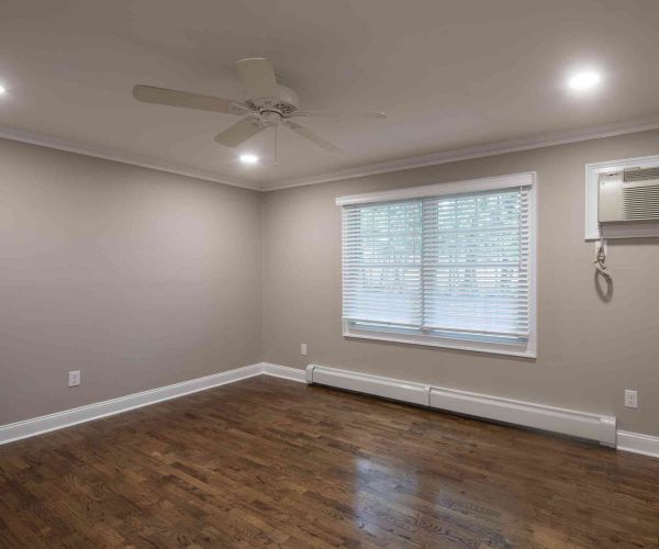 Empty room at Westwood Manor with hardwood floors, beige walls, ceiling fan, window blinds, and wall-mounted air conditioner.