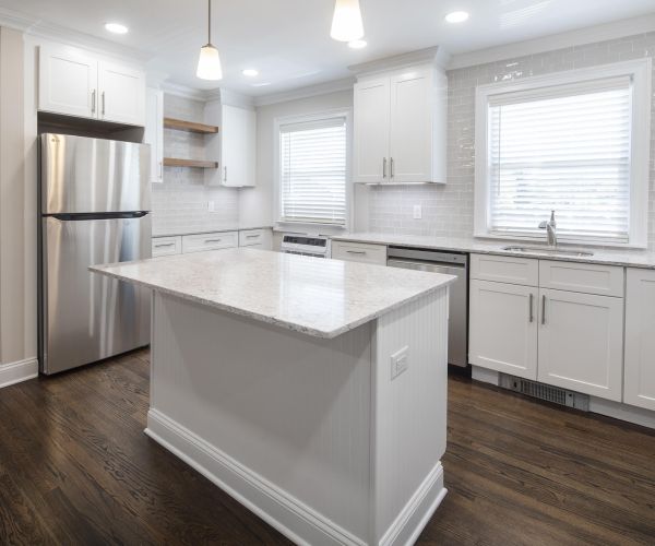 Modern kitchen with white cabinets, stainless steel appliances, island, and dark wood floors.
