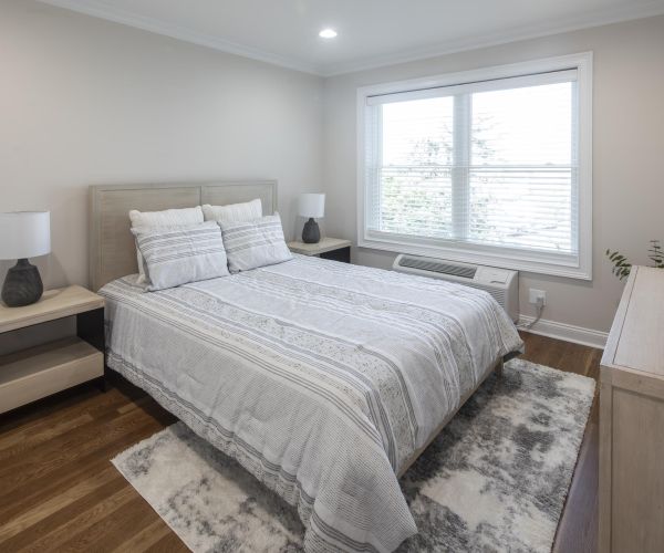Modern bedroom with a double bed, two nightstands, lamps, a dresser, and a large window with blinds.