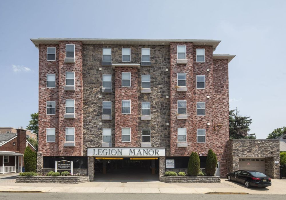 Four-story brick apartment building with sign reading "Legion Manor" above the entrance and driveway.